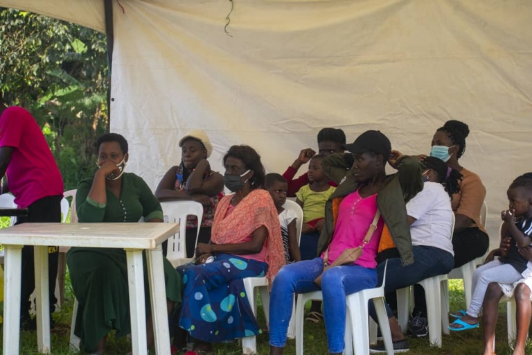 A group of community members gathered under a white tent during a Held at Heart Uganda outreach event.